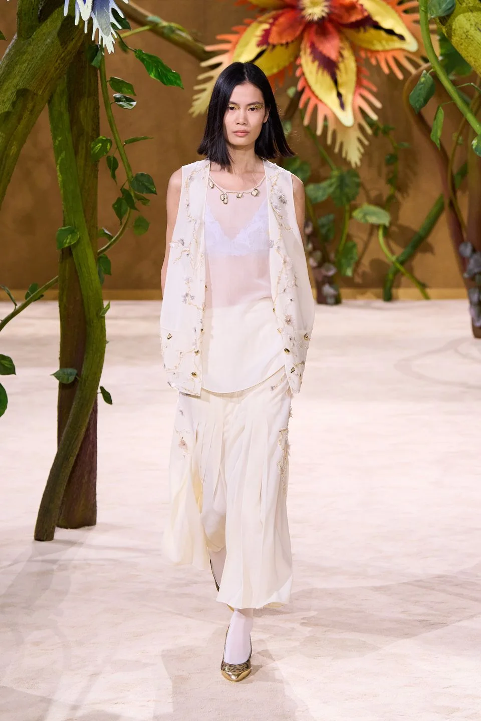 Claros e neutros suaves — 43% como cor dominante: off-white, creme, bege, nude, pêssego, rosa claro, azul gelo, verde-água e palha formam a base mais recorrente da coleção. Eles sustentam a leveza couture e deixam os detalhes botânicos aparecerem.